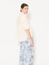 Camisa color crema de poplin liso, con acceso frontal a través de cartera oculta con seis botones forrados en tela base y un botón petra en el pie de cuello. Las mangas cortas finalizan en puño con elástico. Incluye un bolsillo plaqué con atraques triangulares para refuerzo y bordado marcario JCH en el lateral inferior.