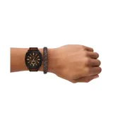 Set de reloj Fossil modelo Machine con caja negra, esfera marrón y correa de cuero marrón. Incluye una pulsera trenzada de cuero marrón y negro.