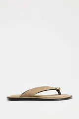 Sandalia plana color beige, con tira de serraje para el dedo y adorno metálico dorado.