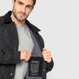 Chaqueta negra acolchada con diseño de rombos, cuello de pana y cierre frontal con botones a presión.