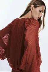 Blusa color ladrillo con textura de lunares, cuello redondo con cordón ajustable con borlas, manga larga abullonada con puños elásticos y ruedo elástico.