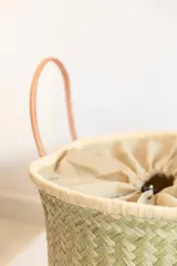 Bolso tipo tote de raffia natural con diseño tejido, interior forrado en tela fucsia y doble asa de cuero color beige. Tiene base rectangular y detalles de cuero en las esquinas inferiores.