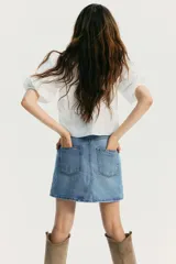 Blusa blanca de algodón con textura de lunares. Tiene escote redondo con lazo, botones en el frente, mangas tres cuartos abullonadas, cordón ajustable en la cintura y peplum.