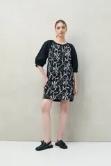 Vestido corto blanco de algodón con bordado floral en relieve, escote redondo con abotonadura frontal y mangas amplias.