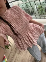 Blusa a cuadros color salmón y blanco, con cuello alto fruncido, mangas cortas con volados y corte peplum con frunces en la cintura.