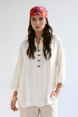 Sobrecamisa beige de corte recto, cuello mao y mangas 3/4. Presenta cierre frontal con botones de madera y bolsillos laterales.