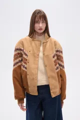 Chaqueta holgada de poliéster en color tostado con forro de corderito, cuello de solapa y cierre frontal con botones. Presenta mangas con apliques de diseño geométrico en tonos marrones y azules.