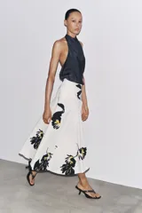 Falda midi de tiro alto confeccionada en hilatura de algodón color blanco con estampado floral en negro y amarillo. Tiene cierre con cremallera oculta en la costura y detalle de botones en la cintura.