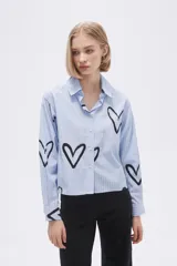 Camisa celeste a rayas verticales blancas, con cuello clásico, cierre frontal con botones y estampado de corazones negros.