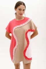 Vestido corto de algodón, con bloques de color en tonos pastel (amarillo claro, beige y rosado pálido) unidos por volados fruncidos en tonos marrón claro y amarillo. Presenta cuello redondo y mangas cortas.