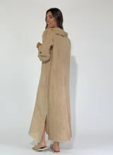 Vestido largo color beige de lino, con escote en V con volados y mangas 3/4 con puños elásticos. Tiene aberturas laterales en el ruedo.