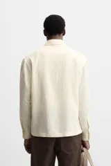 Camisa color crema de corte relaxed fit, confeccionada en tejido con mezcla de viscosa. Tiene cuello solapa, manga larga con puños abotonados, bolsillo de parche en el pecho y cierre frontal con botones.