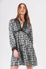 Vestido corto con estampado abstracto en tonos celeste, negro y blanco. Tiene escote en V con ribete de terciopelo negro, mangas largas con puños fruncidos y corte escalonado en la falda.