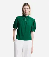 Blusa verde esmeralda de crepé con cuello alto, botones dobles y pequeña abertura en el cuello. Tiene mangas cortas abullonadas con botones.