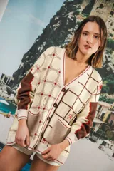 Cardigan oversized de tejido jacquard color crema con diseño de cuadrados en marrón y detalles bordados. Tiene cuello en V, cierre con botones, mangas largas y bolsillos frontales.