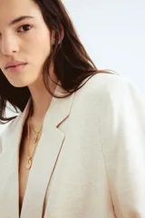 Blazer color crema de lino con doble botonadura, solapas de muesca y bolsillos delanteros ribeteados con solapa. Forrado.
