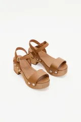 Sandalias con plataforma de madera, tira ancha de cuero color marrón claro en la parte delantera y pulsera al tobillo con hebilla.