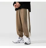 Pantalón de jogging marrón con cintura elástica y cordón ajustable. Presenta una franja vertical blanca a lo largo de la pierna.