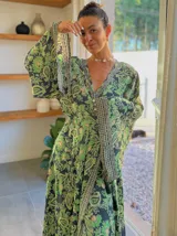 Kimono largo de seda con estampado floral en tonos verde, marrón y beige. Tiene mangas amplias y corte cruzado con lazo ajustable en la cintura.