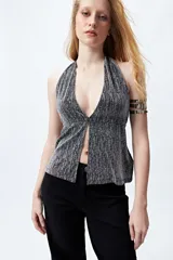 Top halter negro con escote profundo y destellos metalizados. El frunce frontal realza la silueta y el tajo sutil aporta un toque atrevido.