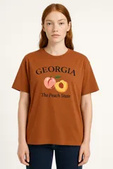 Remera color marrón con estampado de la palabra Georgia, dos duraznos y la frase "The Peach State".