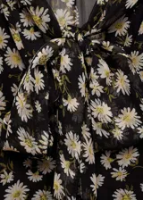 Blusa de gasa negra con estampado de margaritas blancas, cuello pico con lazo y cierre de botones frontal.