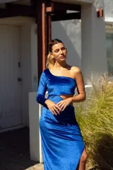 Vestido largo de terciopelo azul eléctrico, con un hombro descubierto, una manga larga, abertura lateral y falda con frunces.