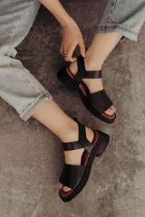 Sandalias bajas color arena, con tiras anchas de cuero y hebilla lateral.