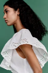 Blusa blanca de algodón con secciones en broderie. Modelo con mangas cortas de volados y cuello redondo con abertura de cerradura y botón oculto en la nuca.