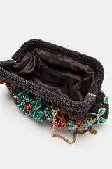 Bolso de mano con cuerpo en abalorios negros y diseño floral multicolor. Tiene asa de anillas metálicas extraíble en forma de bandolera, bolsillo interior y forro interior. Cierre mediante clip.