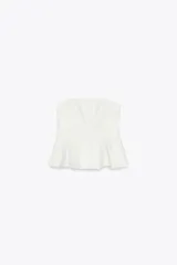 Top blanco de tejido elástico, sin mangas y con escote recto. Tiene corte peplum en la parte inferior y cierre con cremallera oculta en la costura.