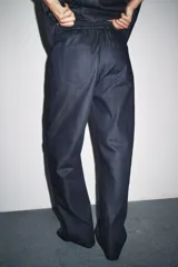 Pantalón de denim azul oscuro, de tiro medio y corte ancho, con cintura elástica en la parte trasera y cierre frontal con cremallera y botón.