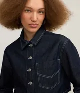 Camisa cropped de jeans azul oscuro, con cuello inglés, mangas largas, bolsillo en el pecho, pespuntes contrastantes y cierre con botones.