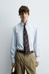Camisa celeste de algodón con estructura twill, corte regular, cuello solapa, manga larga con puños abotonados y cierre frontal con botones.