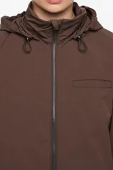 Gabardina midi de corte línea A en color bordó, confeccionada en mezcla de algodón técnico. Presenta cierre frontal con cremallera metálica, cuello subido con capucha integrada y mangas largas ajustables con botones de presión en los puños. Incluye bolsillos laterales y aberturas con botones en los costados.