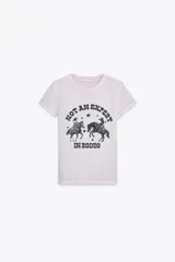 Camiseta color gris claro con cuello redondo, mangas cortas y hombros caídos. Estampado frontal con dos jinetes a caballo y la frase "Not an expert in rodeo".