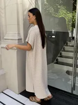 Vestido largo de tejido a rayas horizontales en tonos beige y blanco, con escote en V y mangas cortas tipo murciélago. Presenta tajos laterales en el ruedo.