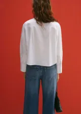 Camisa blanca crop de popelina de algodón, corte regular, manga larga con puños abotonados, cuello camisero y cierre frontal con botones.