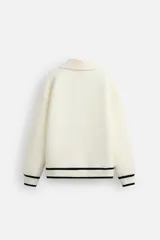 Sudadera color crudo de tejido técnico con cuello alto y cierre de cremallera. Tiene manga larga, corte relaxed fit, bolsillo tipo canguro y rib en puños y bajo con rayas negras.