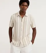 Camisa de manga corta para hombre, confeccionada en tejido texturizado de mezcla de algodón y poliéster. Presenta un diseño de rayas verticales en tonos beige y blanco, cuello tradicional y cierre frontal con botones.