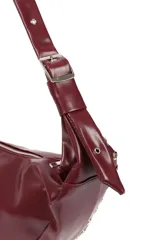 Cartera tipo hobo color bordó de cuero sintético, con cierre superior y asa regulable. Decorada con ojales metálicos plateados.