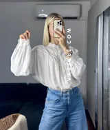Camisa blanca de mangas largas con detalles de encaje en el cuello y en el frente.
