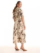 Vestido maxi de crepe color beige con estampado floral en tonos marrones y negros. Presenta cuello a la base, escote en V, abertura central con botones y cintura con lazo de ajuste y hebilla.