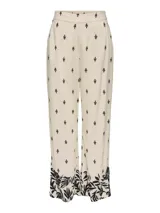 Pantalón de pierna ancha color crema con estampado de hojas negras, cintura elástica trasera y bolsillos frontales.