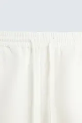Pantalón color arena de corte recto, confeccionado en tejido de algodón y lino. Cuenta con cintura elástica ajustable con cordón, bolsillos delanteros y traseros de parche.