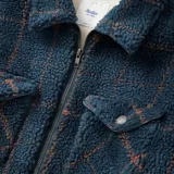 Campera tipo camisa de sherpa azul con diseño a cuadros marrones, cierre frontal con cremallera, cuello clásico y dos bolsillos con solapa abotonada en el pecho.