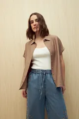 Camisa color marrón claro, de manga corta con puños arremangados, cuello clásico y cierre frontal con botones.