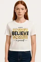 Remera blanca de corte clásico con estampado frontal que incluye la frase 'Always Believe in yourself' sobre un fondo con diseño de cebra en tonos dorados y negros.