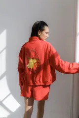 Campera bomber color coral confeccionada en mezcla de algodón y lino, con cierre frontal y bordado grande en la espalda inspirado en la colección La Verdulería.