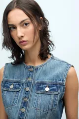 Chaleco crop de denim celeste, sin mangas, con cuello redondo, cierre frontal con botones metálicos, dos bolsillos con solapa en el pecho y corte ajustado.